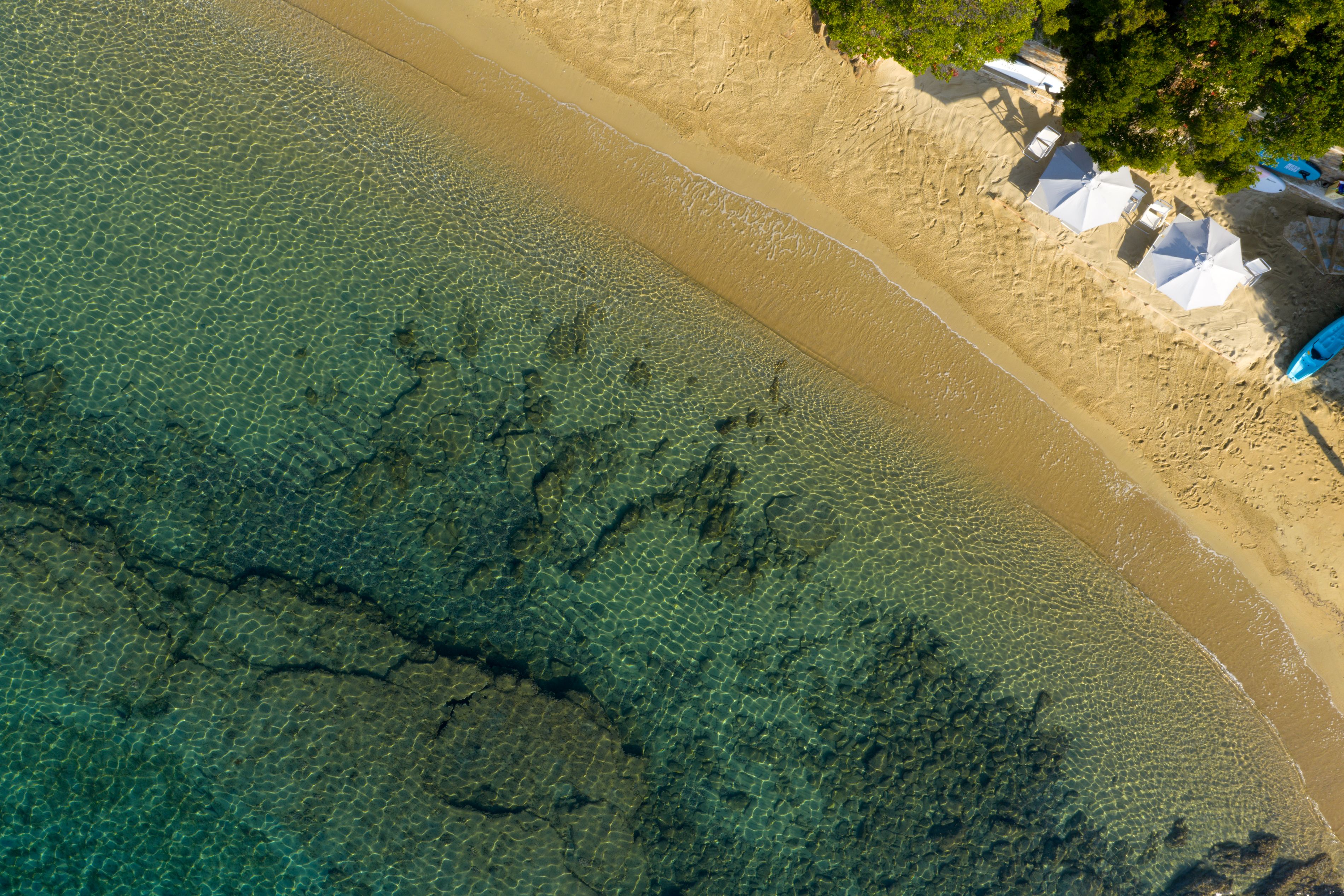 Clear, shallow water over golden sand with the dark rock shelf offshore, seen from above