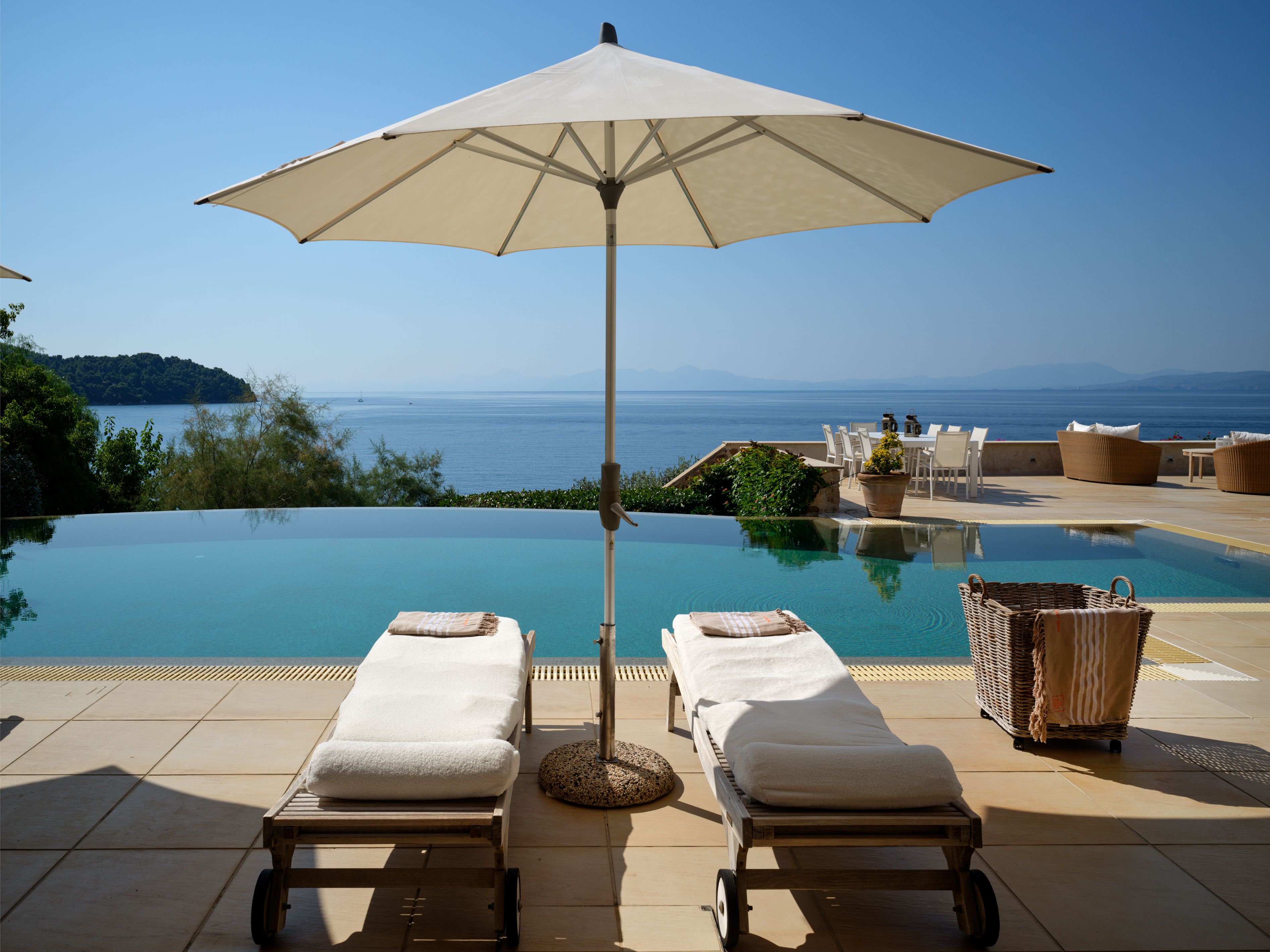 Two sunbeds and an umbrella at the edge of the infinity pool, the sea beyond