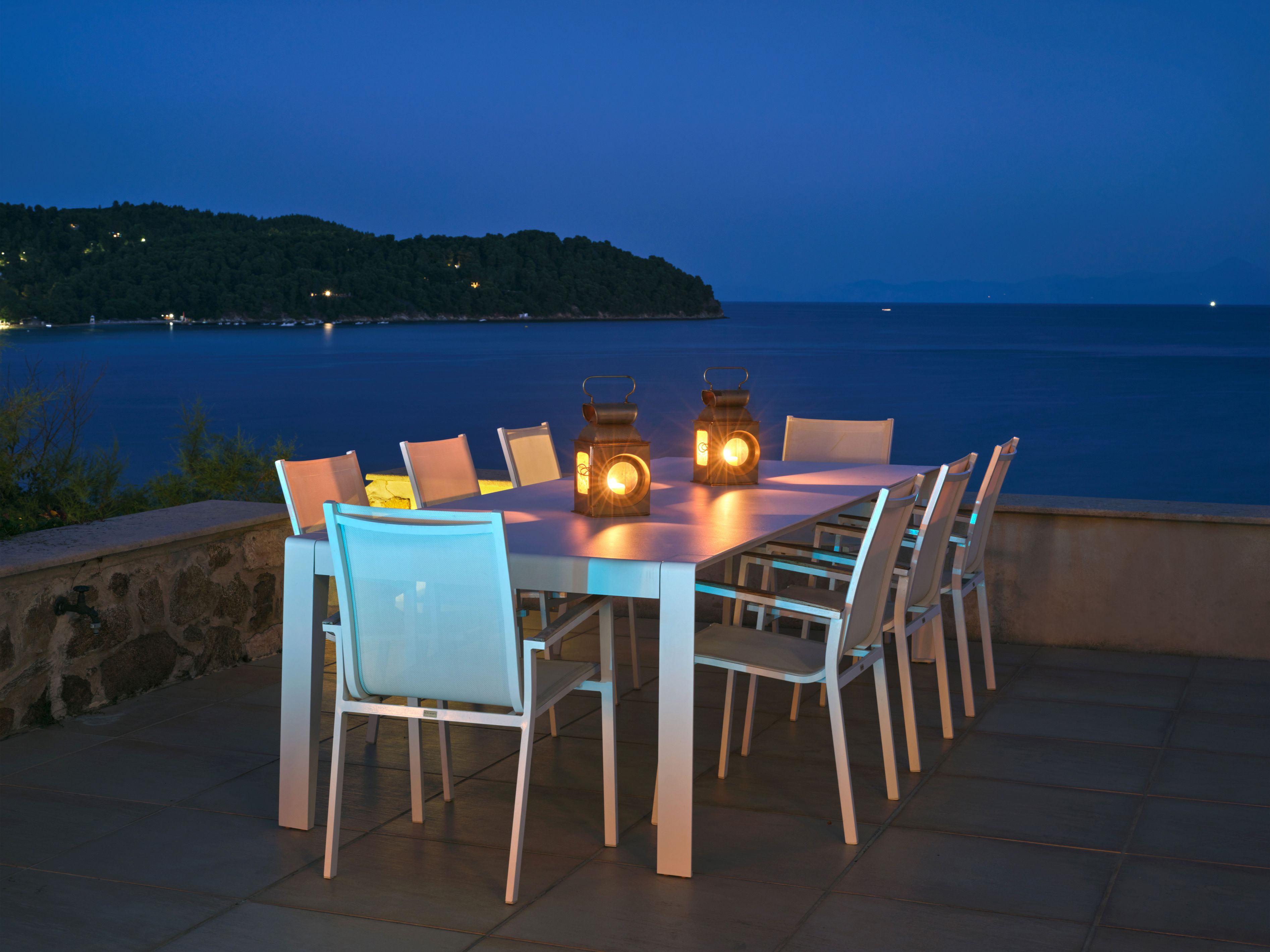 The dining terrace laid for dinner at night, the bay beyond