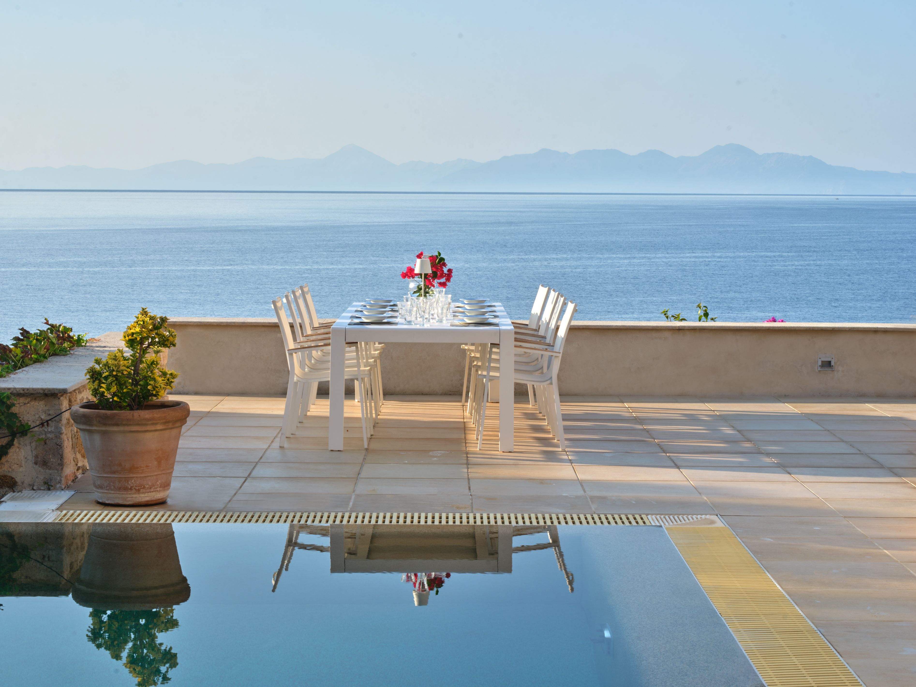 A table laid with flowers beside the pool and the sea